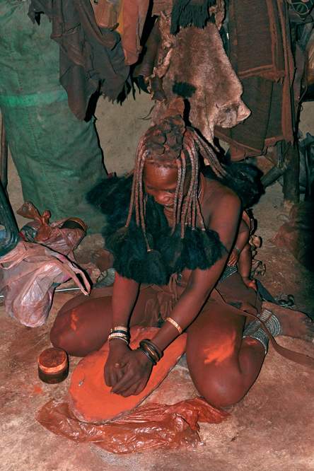 2011-11-13_11-58-18.jpg - Im Dorf der Himba (Aus Tierfett und feingemahlenem Rotsandstein wird die Paste gemixt, mit der sich die Himba-Frauen einreiben; eine Kräutermixtur wird an Fußgelenken und Hals vorher eingerieben. Auf dem Rücken ist das Baby ständig dabei.)